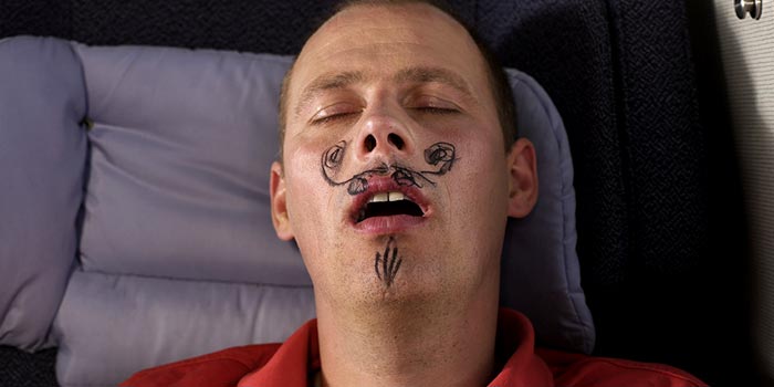 A sleeping man who has had a mustache drawn on his face.