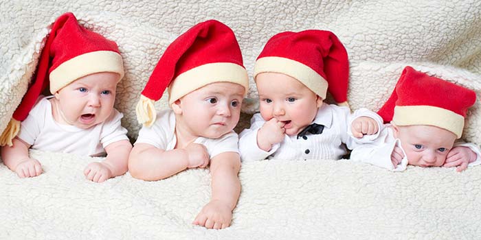 Four newborn babies wearing Santa hats and looking adorable.